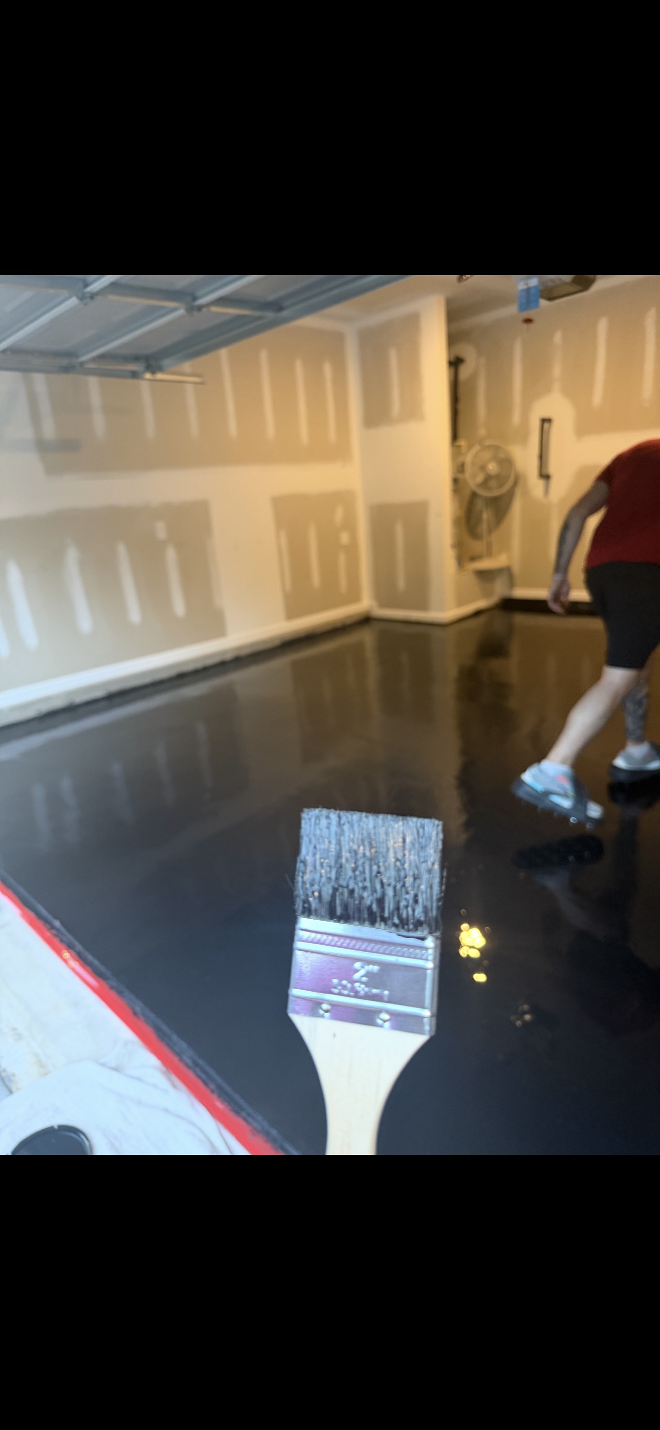 Coating brush above a freshly applied black resin layer in a residential garage