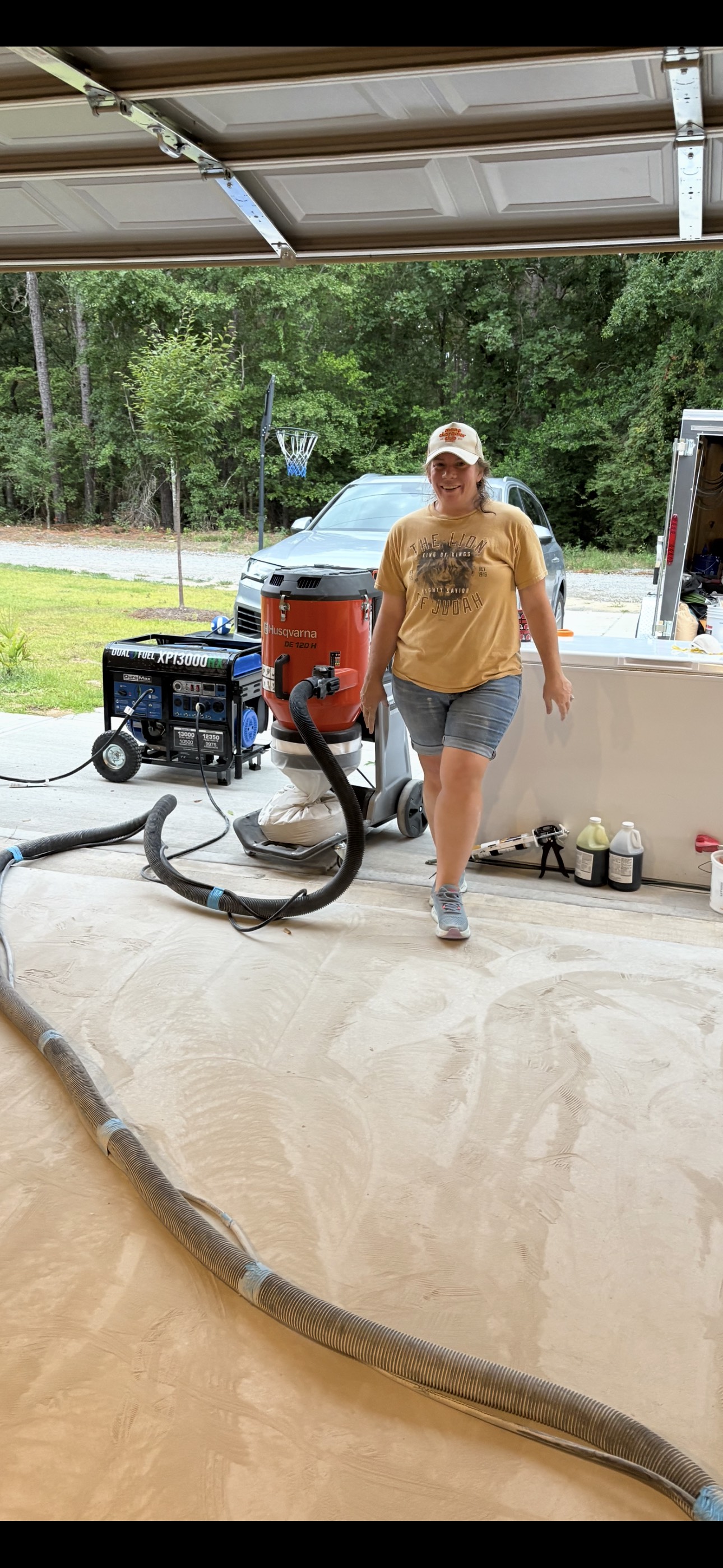 Crew member standing with concrete grinding and dust-control equipment in a garage